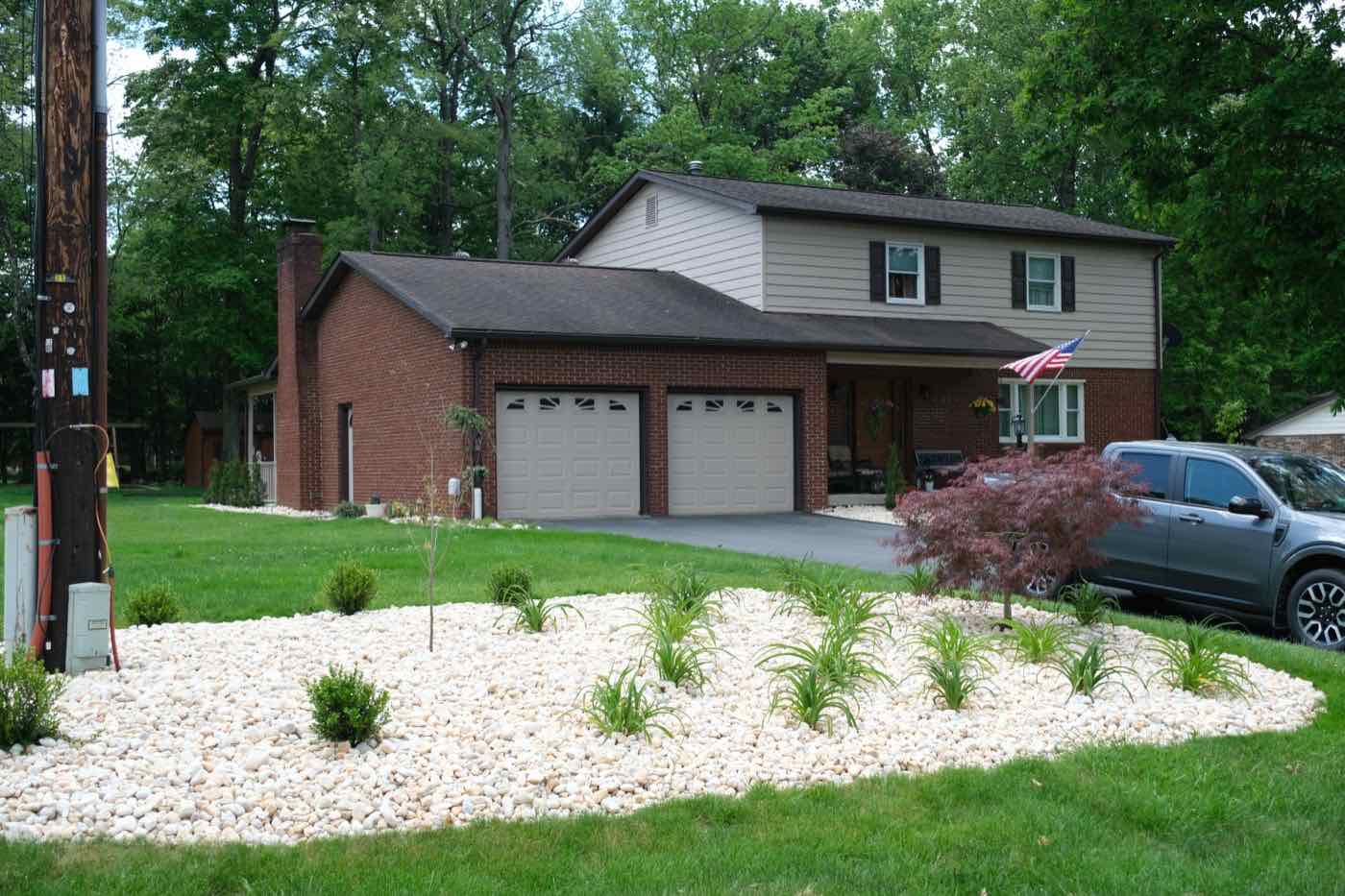 White stone beds with daylilies in front of a brick home, installed by Luke’s Landscaping